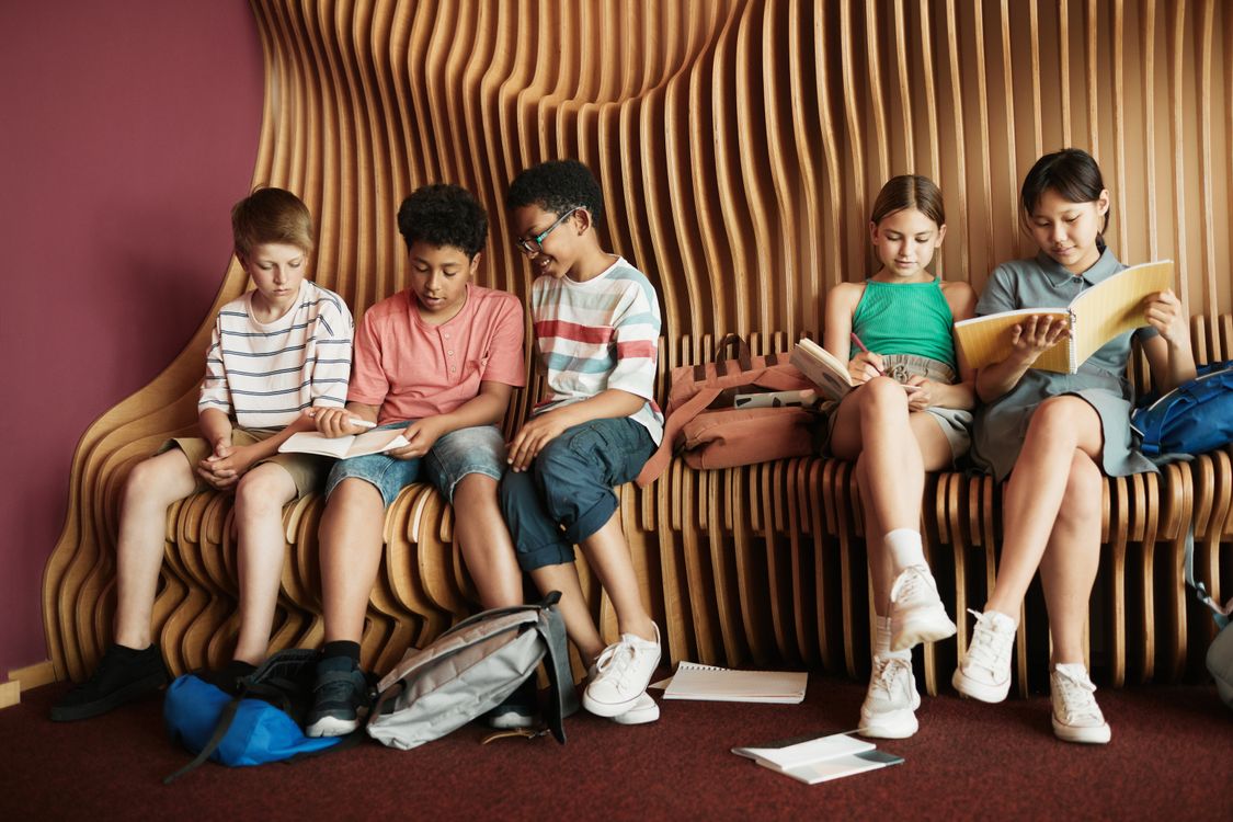 Un groupe d'enfants d'origines diverses lisant un livre ensemble sur un banc